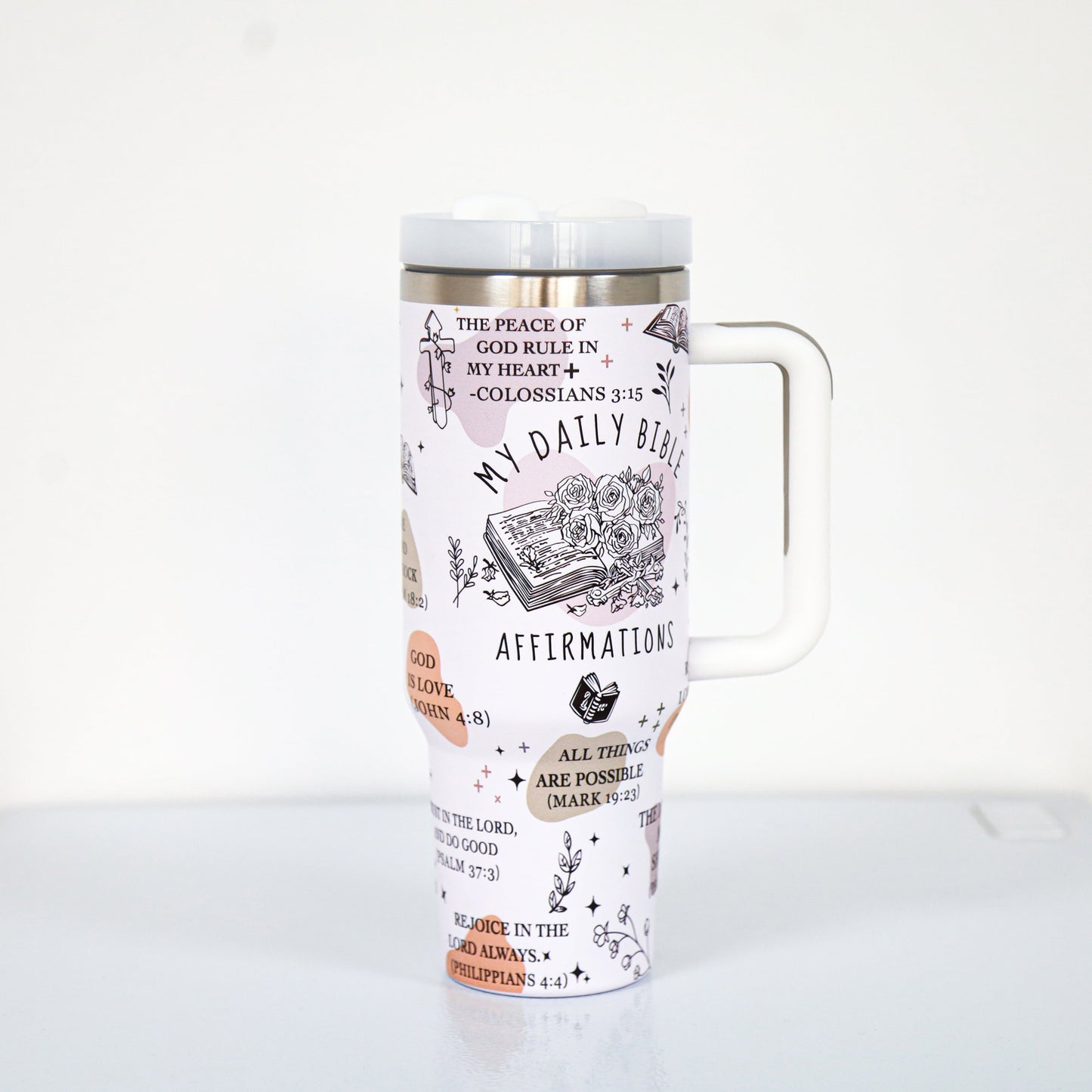 A pastel pink tumbler with a white handle and lid, decorated with Bible-themed affirmations and scriptures such as "My Daily Bible Affirmations," "All things are possible (Mark 9:23)," and floral illustrations surrounding a sketch of an open Bible.