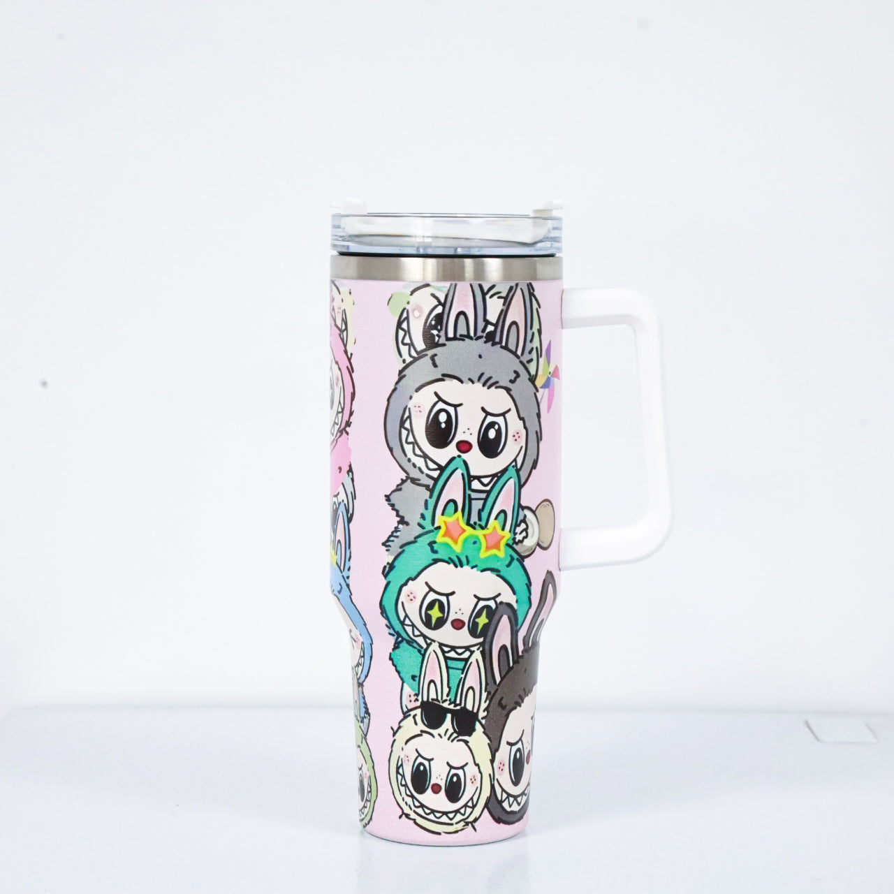 A pastel pink tumbler with a white handle and lid, featuring Labubu characters in antler and bunny costumes, with a clear straw lid and stainless steel rim.