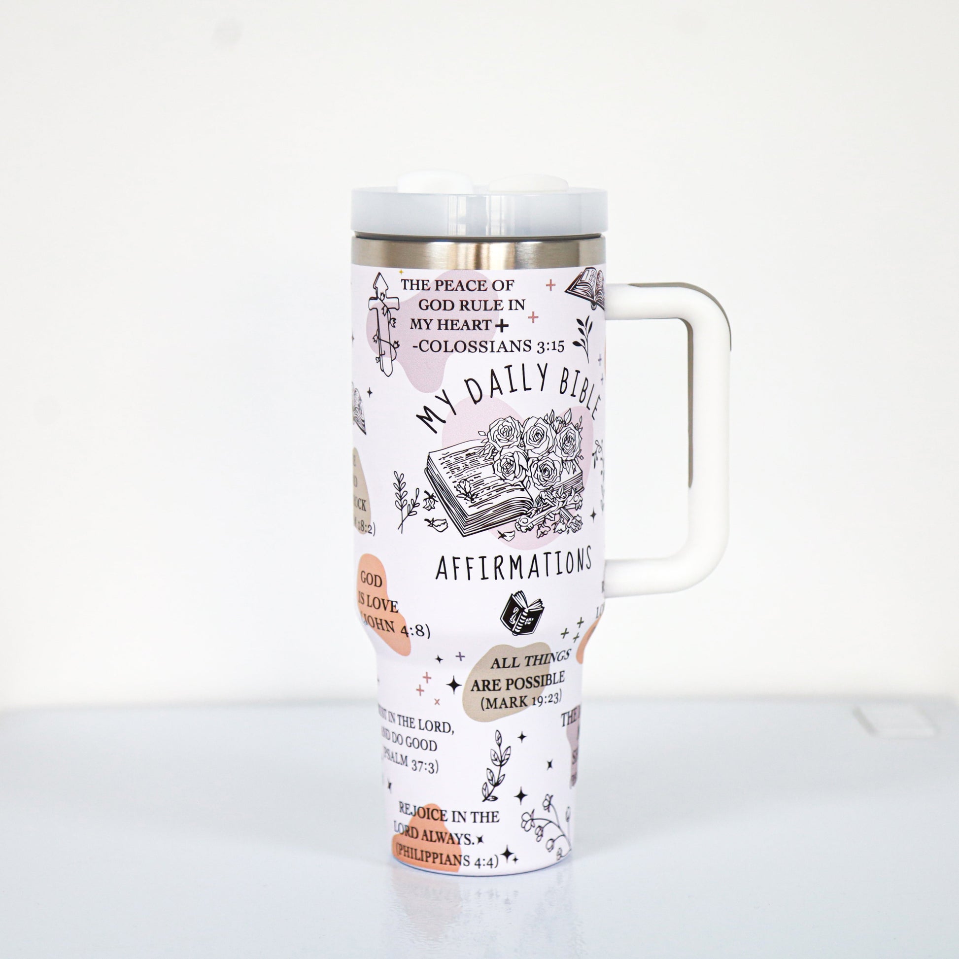 A pastel pink tumbler with a white handle and lid, decorated with Bible-themed affirmations and scriptures such as "My Daily Bible Affirmations," "All things are possible (Mark 9:23)," and floral illustrations surrounding a sketch of an open Bible.