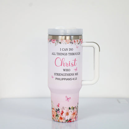 A pastel pink tumbler with a white handle and lid, featuring the Bible verse "I can do all things through Christ who strengthens me – Philippians 4:13," surrounded by floral and butterfly illustrations at the top and bottom.